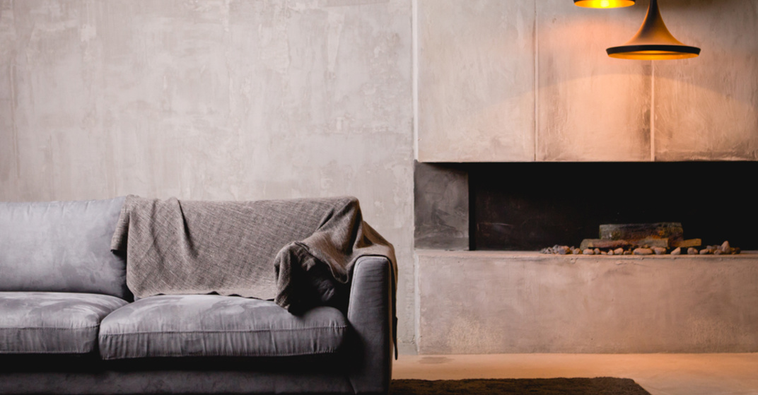 Cleanes, modernes Wohnzimmer mit grauer Couch und brauner Decke vor Wand aus Sichtbeton und betoniertem offenem Kamin