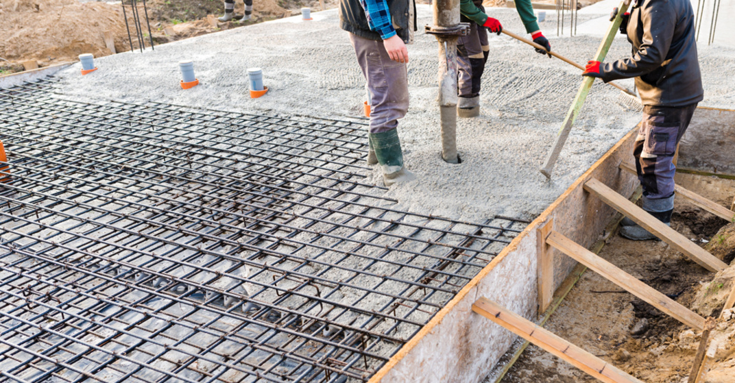 Bauarbeiter stehen auf frisch betonierter Kellerdecke mit Stahlbewehrung und verteilen flüssigen Beton