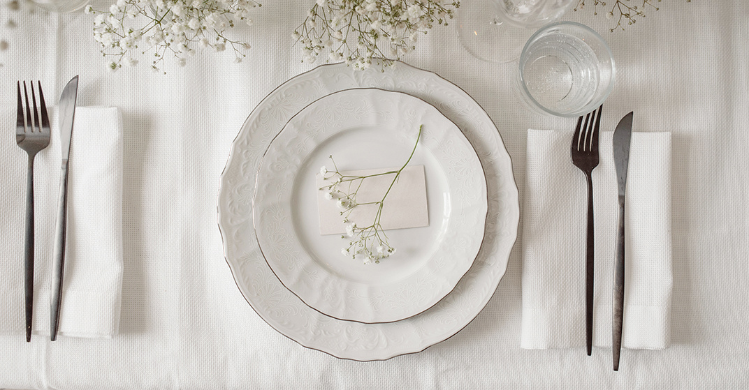 Elegantes weißes Porzellangedeck auf weißem Tischtuch dekoriert mit zartem Schleierkraut aus der Vogelperspektive.