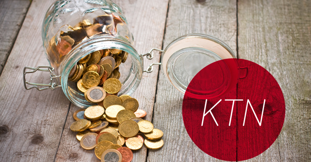 Gekipptes Einmachglas mit verschiedenen Euro- und Centmünzen liegt umgekippt auf einem rustikalen Holzboden, dazu der Text "KTN" in rotem Kreis.